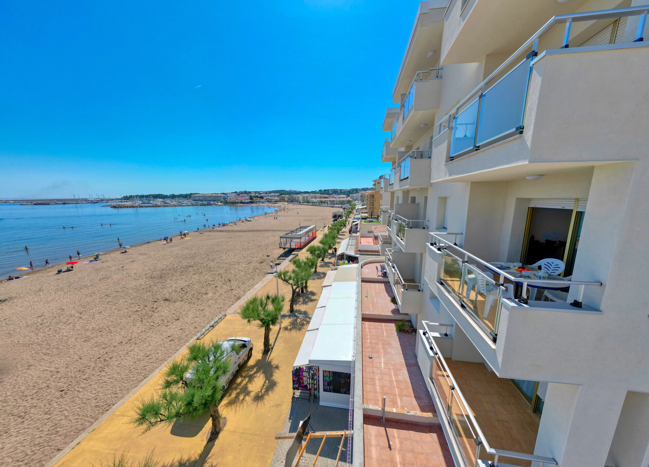 Un hôtel en bord de mer, doté de balcons avec vue sur l’océan, d’une plage de sable et d’un ciel dégagé.