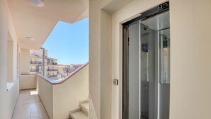 A narrow corridor with a balcony, a glass elevator, and a view of neighboring buildings. - RIELLS: Fully renovated seafront apartment (L'Escala)
