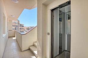 Ein enger Korridor mit einem Balkon, einem Glastauschaufzug und Blick auf benachbarte Gebäude.