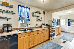 A kitchen with wooden cabinets, a coffee bar, a sink, a stove, and blue curtains. - Walk to Stetson and Historic Downtown DeLand! (DeLand)