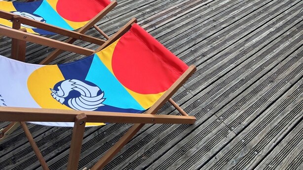 Un pontile in legno con sedie da spiaggia colorate e un piccolo giardino con una pianta e una botte.