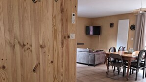 Una parete in legno con una porta scorrevole, un'area pranzo con tavolo e sedie, un divano e una televisione montata a parete.