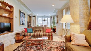 A cozy living room with a sofa, a coffee table, and a TV. There is a fireplace, a bookshelf, and a large window. - Grand Multi-Unit Estate: 2 Mi to Dtwn Minneapolis! (Minneapolis)