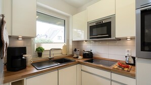 Een moderne keuken met een ingebouwde magnetron, een koffiezetapparaat en een snijplank met tomaten.
