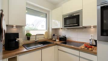 A modern kitchen with a built-in microwave, a coffee maker, and a cutting board with tomatoes.