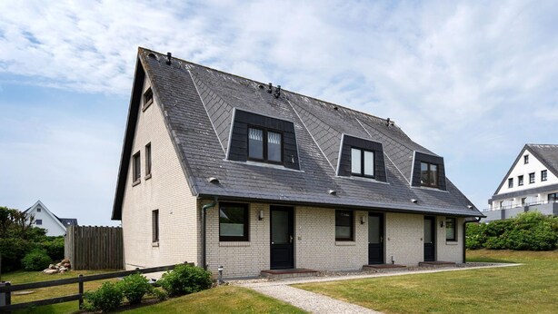Een tweelaags huis met een steile kap, een veranda en een kleine voortuin.