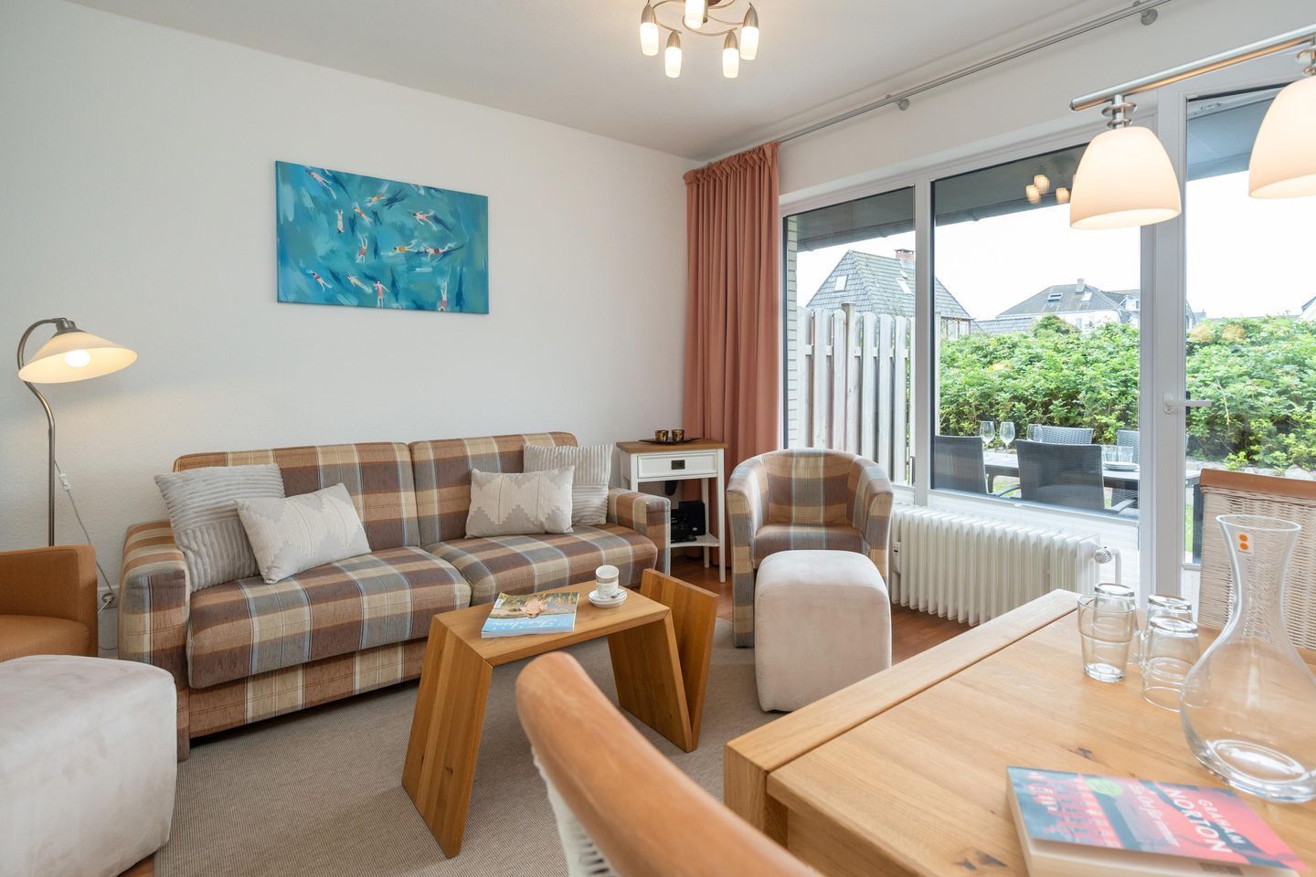 Un salon meublé avec un canapé, une table basse et des fauteuils, un tableau accroché au mur et une vue par la fenêtre.