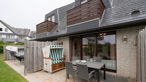 Een terras met een eettafel, een rieten stoel en een surfplank.