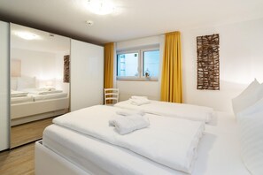Ein Hotelzimmer mit zwei Betten, einem Fenster mit gelben Vorhängen, einem weißen Stuhl und einer Wanddekoration.