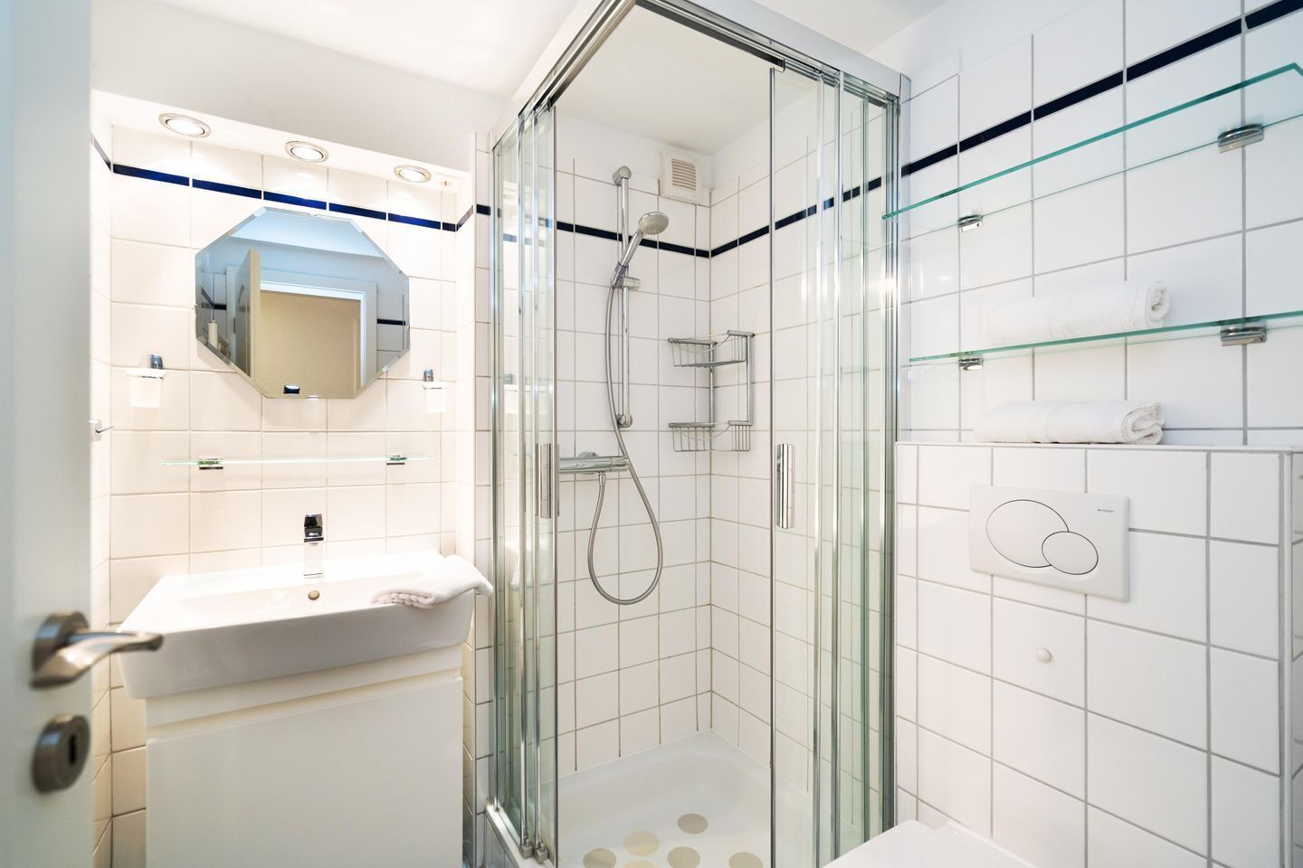 Ein modernes Badezimmer mit einer gläsernen Duschkabine, einem weißen Waschbecken und einem Spiegel darüber.