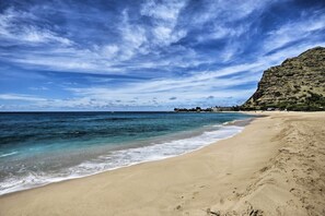 Een strand met helder water, een zandstrand en een berg op de achtergrond.