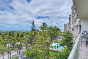 Ein Hotelbalkon mit Blick auf einen Pool, üppiges Grün und eine entfernte Küstenlinie.