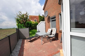 Eine Terrasse mit Tisch und Stühlen, eine Satellitenschüssel und ein Ziegelgebäude mit Garagentor.