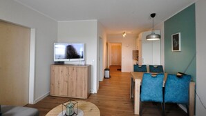 Ein modernes Wohnzimmer mit Fernseher, Holzschrank, rundem Couchtisch und blauen Sesseln.