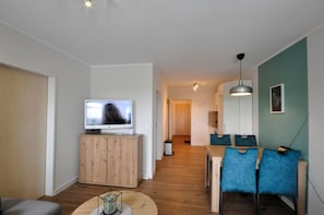 Ein modernes Wohnzimmer mit Fernseher, Holzschrank, rundem Couchtisch und blauen Sesseln.