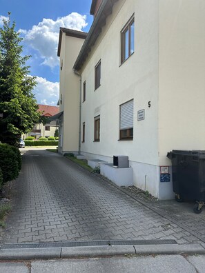 Edificio residencial con entrada pavimentada, contenedor de basura y buzón.