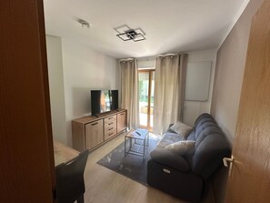 Una sala de estar con sofá, televisor, aparador de madera y puerta corrediza de vidrio que da a un balcón.
