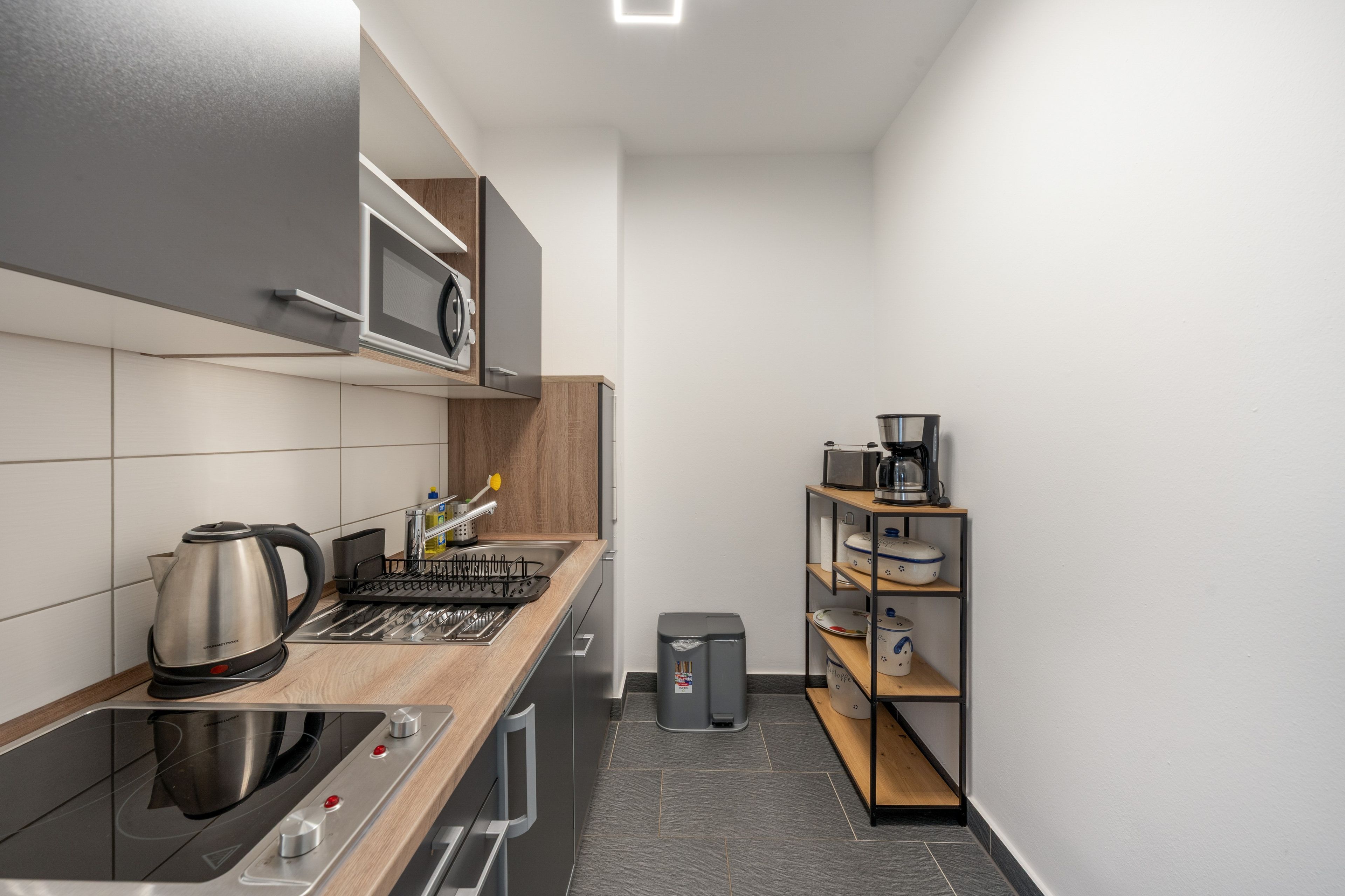 A modern kitchen with a built-in oven, a coffee machine, and a small trash bin.