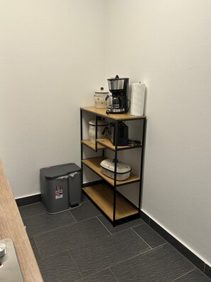 Eine Küchenzeile mit einer Kaffeemaschine, einem Toaster, einem Mülleimer und einem Regal mit Geschirr.