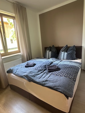 A bedroom with a bed, pillows, a window with curtains, and a radiator. - Saxon Lake Retreat in Birkwitz – Relax Near Saxon Switzerland (Pirna)