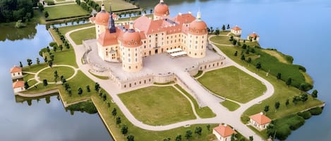 Un edificio grande e histórico con múltiples cúpulas, rodeado de un jardín cuidado y un lago.