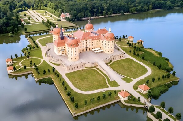 Un edificio grande e histórico con múltiples cúpulas, rodeado de un jardín cuidado y un lago.