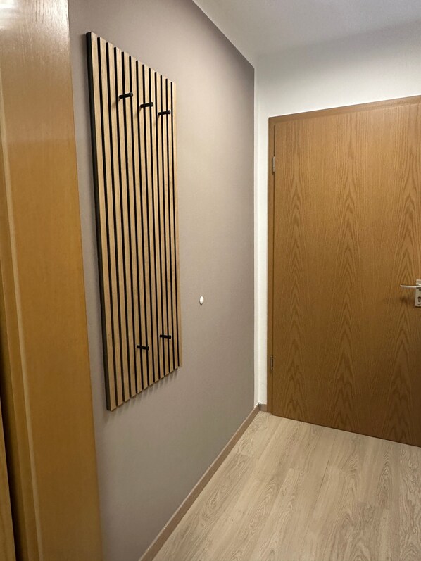 Un pasillo con una puerta de madera, un panel en la pared y un interruptor de luz.