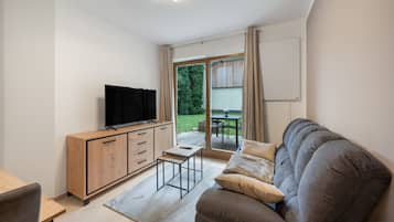 A modern living room with a flat-screen TV, wooden cabinet, grey sofa, and a small table.