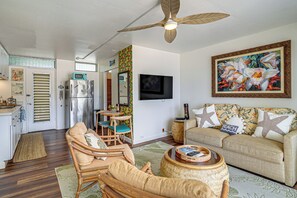 Una sala de estar con ventilador de techo, televisor, sofá y comedor con refrigerador.