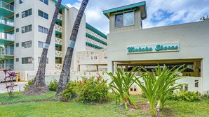 A building with a sign reading 'Makahoa Shores,' surrounded by a well-maintained lawn and palm trees. - Steps to Beach & Pool! Oceanfront Waianae Studio (Waianae)