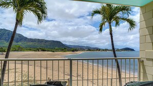A balcony with a view of a beach, palm trees, and mountains. - Steps to Beach & Pool! Oceanfront Waianae Studio (Waianae)