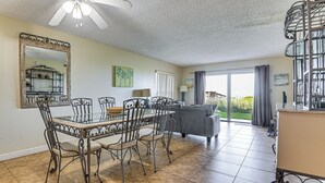 Un espace repas avec une table en verre et des chaises en métal, un canapé, un grand miroir et une vue sur l’extérieur.