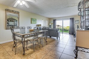 A dining area with a glass table and metal chairs, a sofa, a large mirror, and a view to the outside. - Ocean-View Pool + Boardwalk: Cocoa Beach Condo (Cocoa Beach)