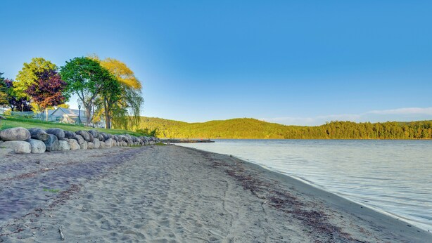 A sandy beach with a stone wall, trees, and a clear sky. - Boat, Fish & Hike! All-Season Schroon Lake Getaway (Schroon Lake)