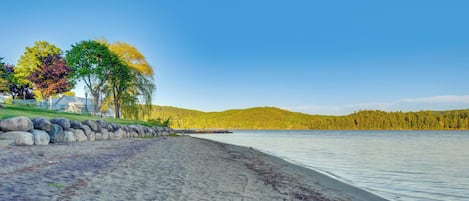 A sandy beach with a stone wall, trees, and a clear sky.