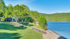 A lakeside property with a grassy area, a wooden bridge, and a small building near the water. - Boat, Fish & Hike! All-Season Schroon Lake Getaway (Schroon Lake)