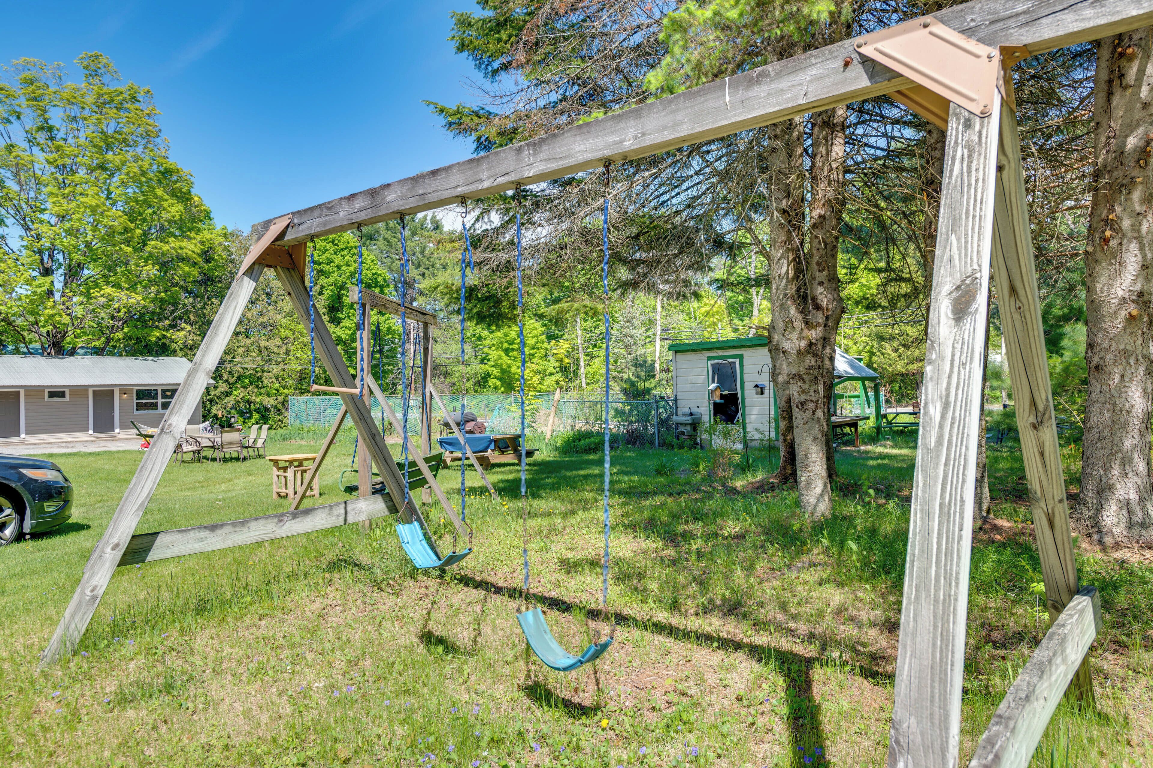 Ein hölzernes Schaukelgestell in einem Garten mit Haus, Bäumen und Rasen.