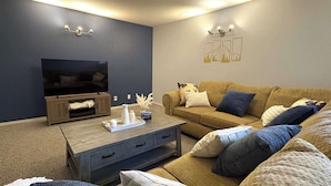 A living room with a TV, wooden coffee table, sofa, and wall-mounted lights. - Fernie - Riverside Way 1230 (Fernie)
