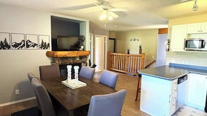 A dining area with a wooden table and chairs, a fireplace, and a television in the background. - Fernie - Riverside Way 1230 (Fernie)