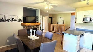 A dining area with a wooden table and chairs, a fireplace, and a television in the background. - Fernie - Riverside Way 1230 (Fernie)