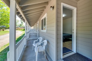 A covered porch with two white plastic chairs, a bed in the adjacent room, and a door leading inside. - Cozy Room Near Schroon Lake Marina, Town & Beach! (Schroon Lake)