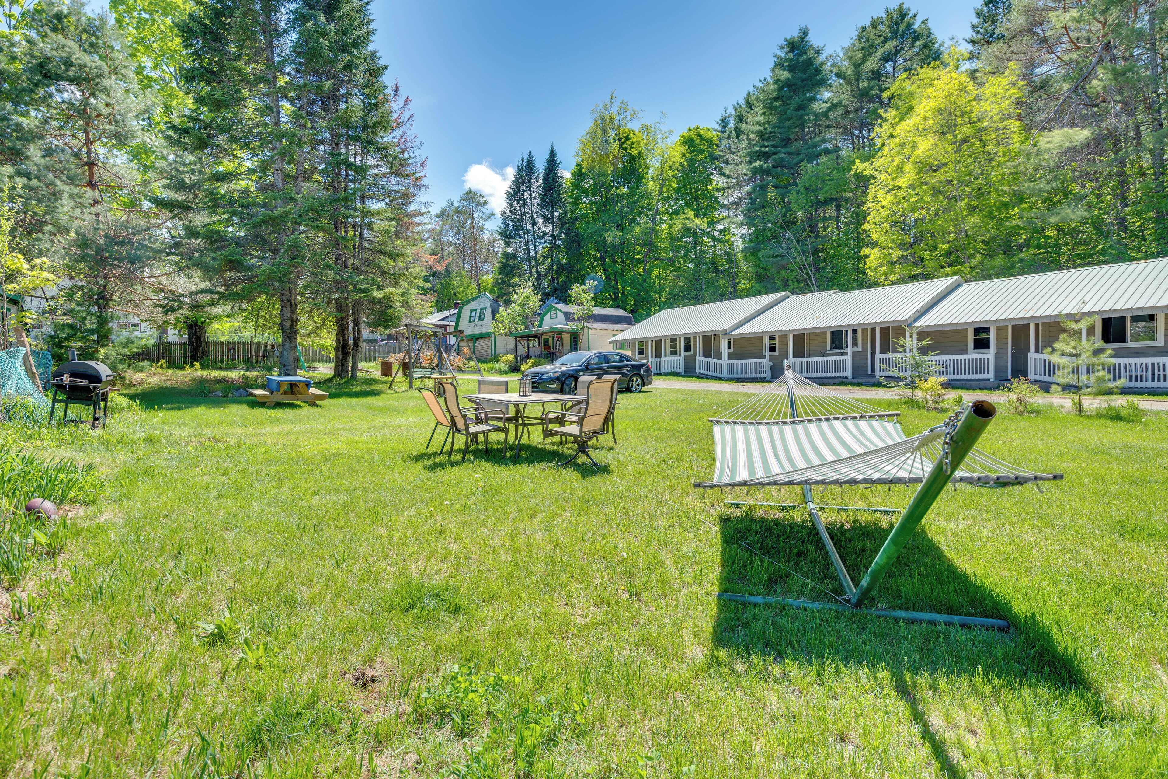 A grassy area with a hammock, a picnic table, and a barbecue grill.