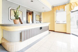 Et receptionsområde med skranke, en potteplante, et indrammet billede og et vindue med gardiner.