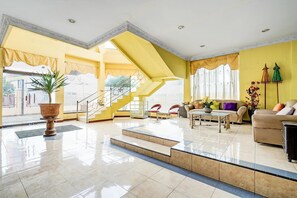 En rummelig lobby med trappe, en stor plantekasse og et siddeområde med sofa og sofabord.