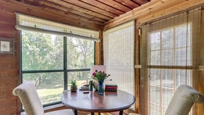 A wooden interior with a round table, two chairs, a vase with flowers, and books.