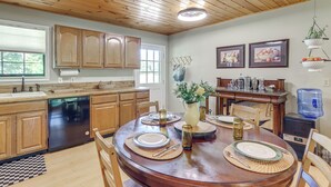 A kitchen with wooden cabinets, a dishwasher, a dining table set with plates and cutlery, and a water dispenser.