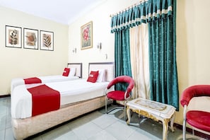 A hotel room with two beds, a red chair, a small table, and curtains.