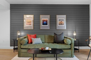 Ein modernes Wohnzimmer mit einem grünen Sofa, drei gerahmten Bildern an der Wand und zwei Beistelltischen mit Lampen.