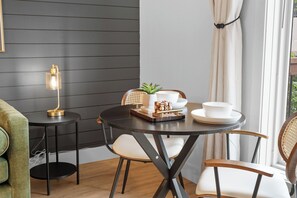 Ein Essbereich mit einem runden Tisch, Stühlen, einer Lampe, einem Topfpflanzen und einem Fenster mit Vorhängen.