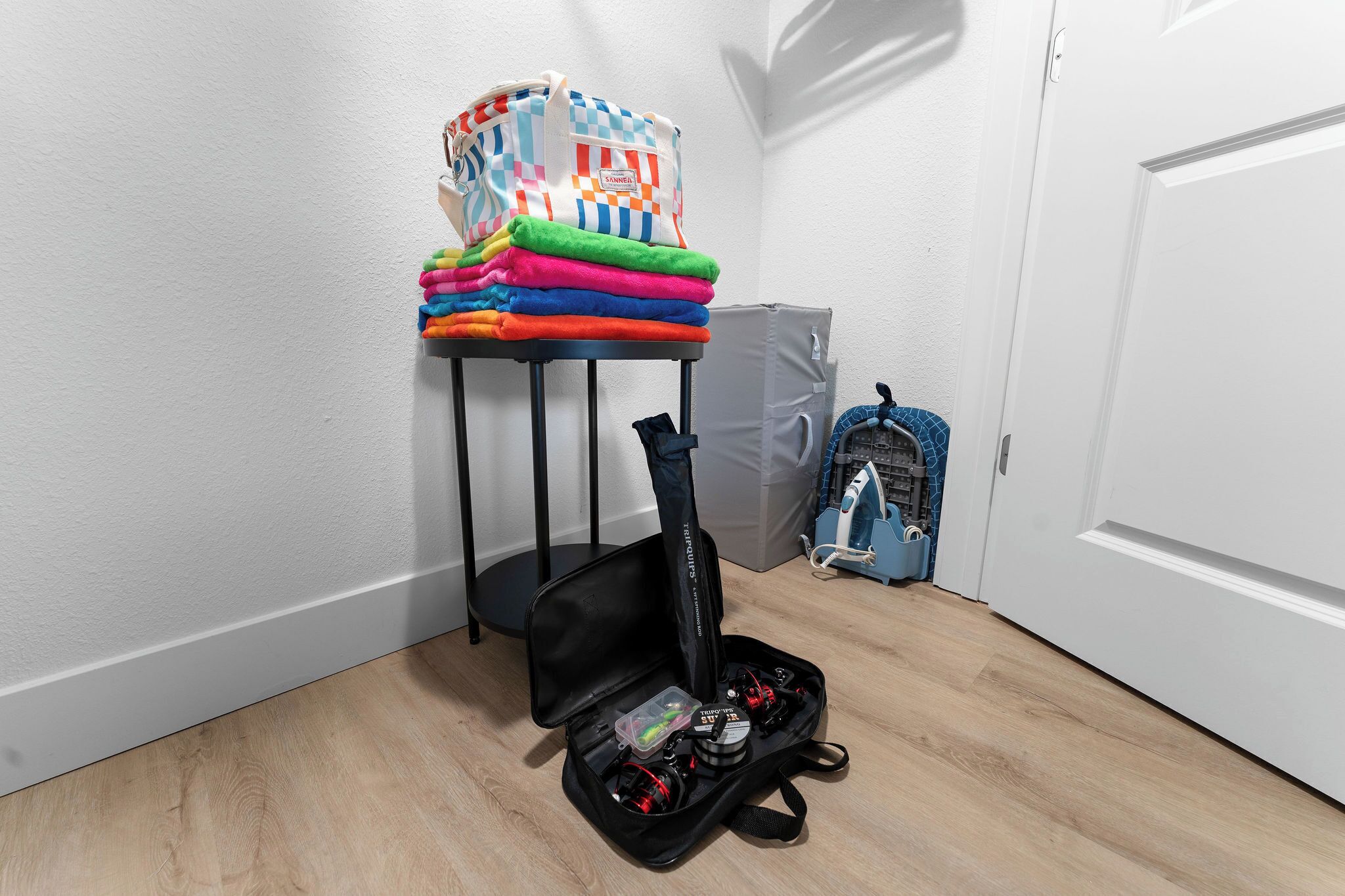 A room with a bed, a bedside table with a bag and folded clothes, a suitcase, and a vacuum cleaner.